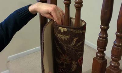 Hand attaching flowered area rug to staircase spindle.