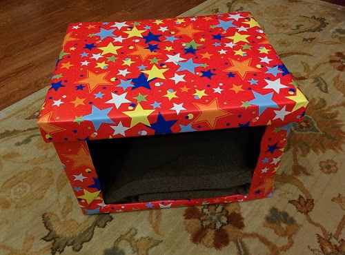 DIY Cardboard cat bed covered in red fabric with different colored stars.